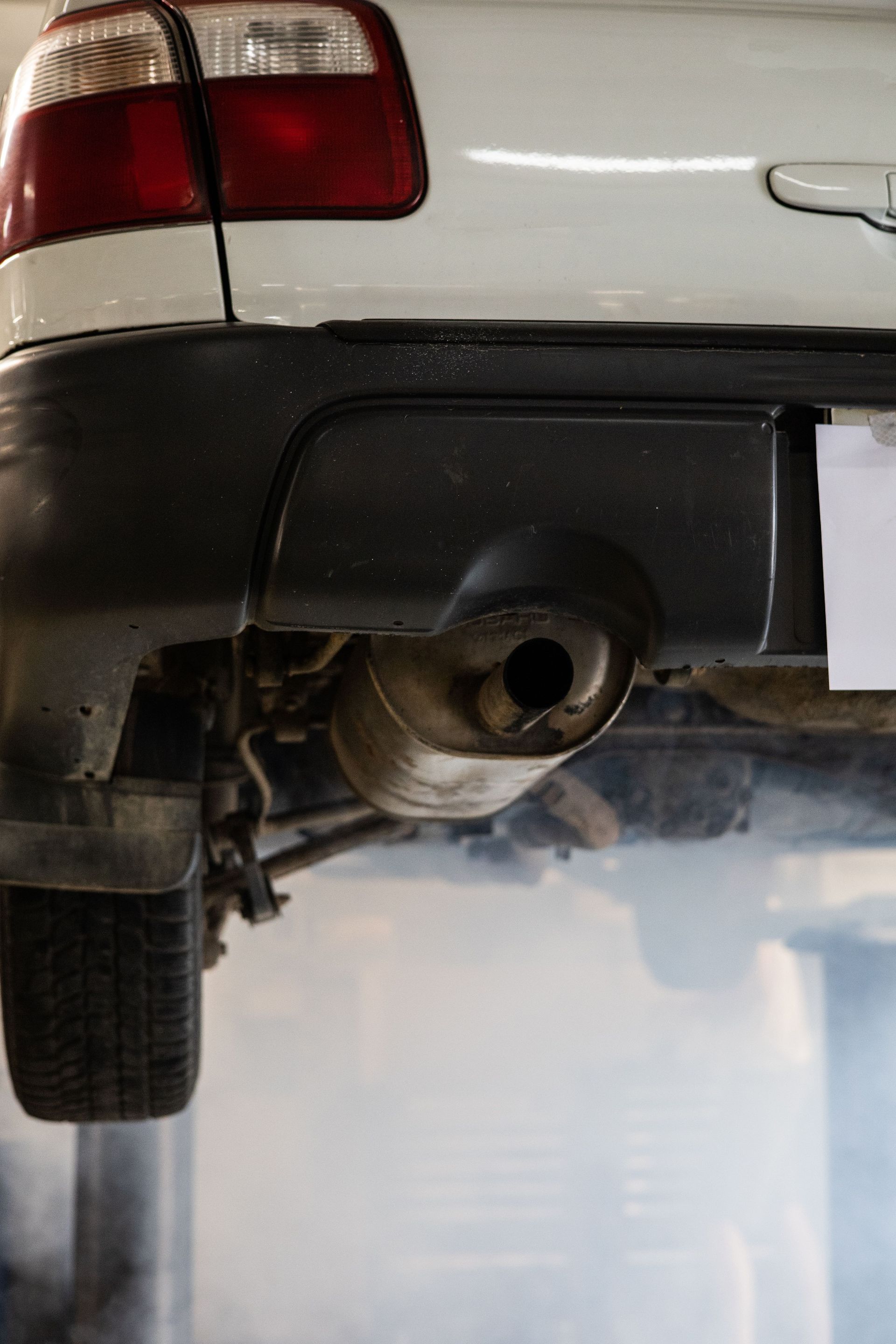 Close-up of a car's exhaust system emitting smoke in an auto repair shop setting.